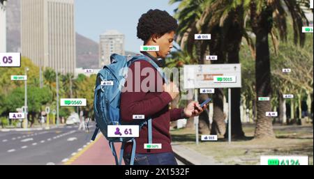 Image de plusieurs barres de notification au-dessus d'un homme biracial tenant un téléphone portable traversant la rue Banque D'Images