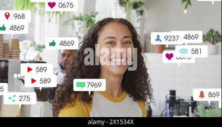 Image de plusieurs barres de notification sur une femme biraciale souriante debout dans un café Banque D'Images