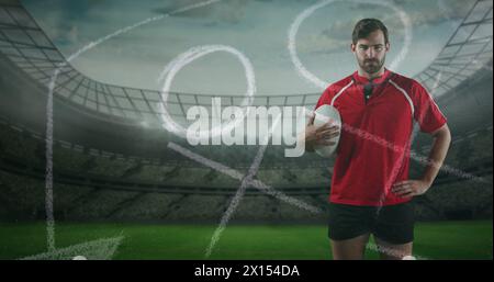 Image d'un joueur de rugby masculin caucasien debout, tenant une balle dans sa main et regardant la caméra wi Banque D'Images