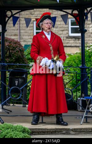 Crier de ville féminine (uniforme coloré de crier de dame) proclamer, faire une proclamation publique bruyante et annoncer - Ilkley, West Yorkshire, Angleterre, Royaume-Uni. Banque D'Images