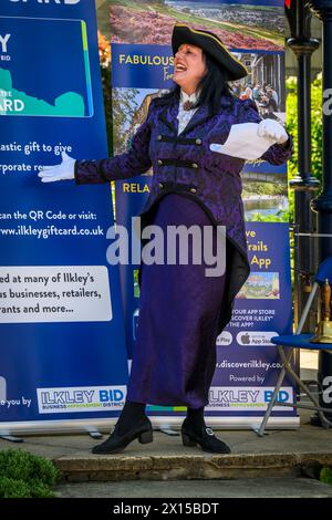 Crier de la ville féminine (vêtements de crier de dame violette) proclamant oyez, faisant une proclamation publique bruyante et annonce - Ilkley, West Yorkshire, Angleterre Royaume-Uni. Banque D'Images