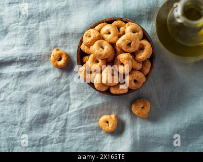 Taralli ou tarallini italien traditionnel dans un bol en bois sur fond de serviette en lin bleu clair. Coup rustique de taralli hors-d'œuvre avec espace de copie. Vue de dessus ou à plat. Banque D'Images