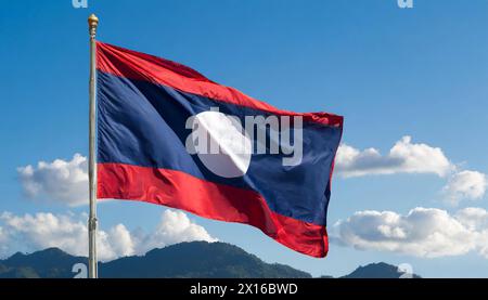 Die Fahne von Laos flattert im Wind, isoliert gegen blauer Himmel Banque D'Images