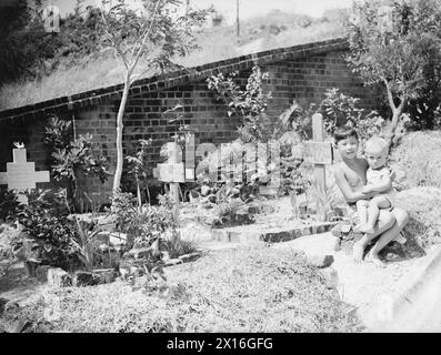 FLOTTE BRITANNIQUE DU PACIFIQUE 1944-1945 - Juan et Dennis Clark, petits internés du Camp Stanley, Hong Kong, sont assis à côté de la tombe de leur petit frère Anthony, né le 2 décembre 1942 dans le camp, et mort de malnutrition trois semaines plus tard. Père était un policier eurasien à Hong Kong lorsque les Japonais sont entrés dans la ville et les ont internés. Les enfants avaient une partie spéciale du cimetière attenant au camp Banque D'Images