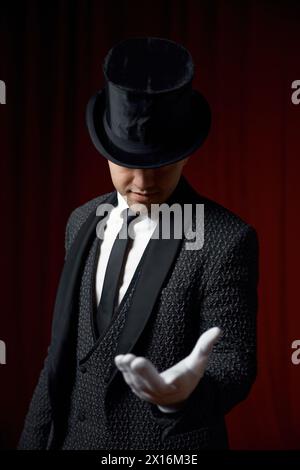 Magicien portant un costume debout avec canne sur scène décoré de rideau de velours rouge Banque D'Images