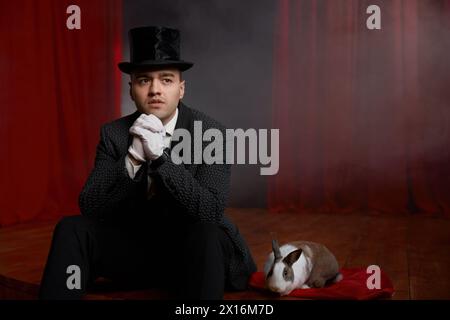 Showman pensif en costume assis sur la scène de théâtre se reposant après le spectacle de magie Banque D'Images