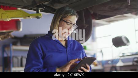 Image de lumière incandescente sur une femme biraciale travaillant dans un atelier de voiture Banque D'Images