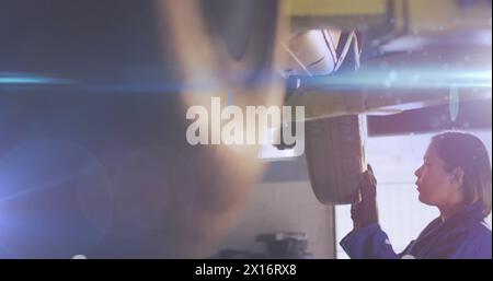 Image de lumière incandescente sur une femme biraciale travaillant dans un atelier de voiture. Petite entreprise, finance, informatique et concept de traitement des données généré numériquement Banque D'Images