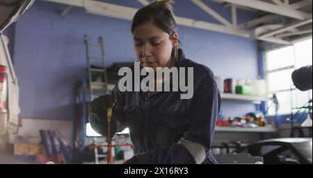 Image de lumière incandescente sur une femme biraciale travaillant dans un atelier de voiture Banque D'Images