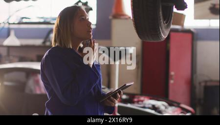 Image de lumière incandescente sur une femme biraciale travaillant dans un atelier de voiture Banque D'Images