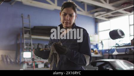 Image de lumière incandescente sur une femme biraciale travaillant dans un atelier de voiture Banque D'Images