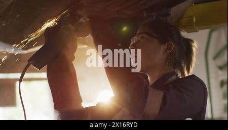 Image de lumière incandescente sur une femme biraciale travaillant dans un atelier de voiture. Petite entreprise, finance, informatique et concept de traitement des données généré numériquement Banque D'Images