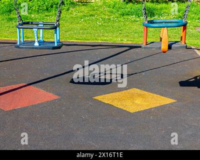 Vue rapprochée des balançoires pour jeunes enfants dans une aire de jeux avec revêtement de sécurité en dessous pour protéger les enfants contre les chutes. Banque D'Images