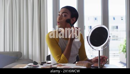 Image de taches lumineuses sur une femme biraciale appliquant le maquillage Banque D'Images