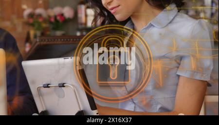 Image de cadenas de sécurité et de traînées de lumière sur une femme biraciale à l'aide d'une tablette numérique dans un bar Banque D'Images