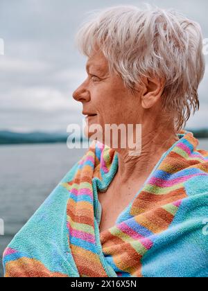 Un nageur en eau libre senior se réchauffe avec une serviette après une baignade rafraîchissante dans le lac d'eau froide - Woman Swim Outdoors Health UK Banque D'Images