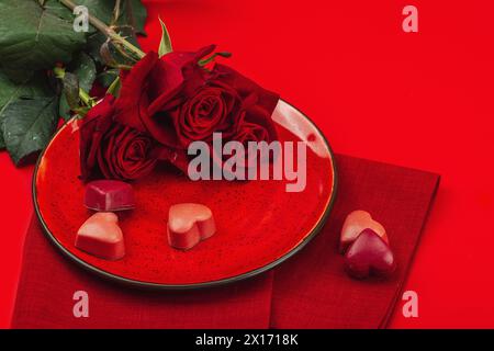 Table de printemps minimaliste avec bonbons au chocolat sucrés. Symbole festif traditionnel, carte de voeux, plat. Fond rouge passion, espace de copie Banque D'Images