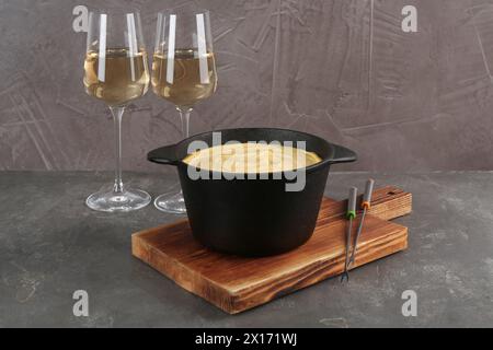 Casserole à fondue avec fromage fondu savoureux, fourchettes et vin sur table grise Banque D'Images