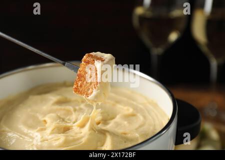 Tremper un morceau de pain dans une casserole à fondue avec du fromage fondu à table, gros plan Banque D'Images