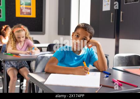 À l'école, un jeune garçon biracial et deux filles se concentrent sur leur travail en classe Banque D'Images