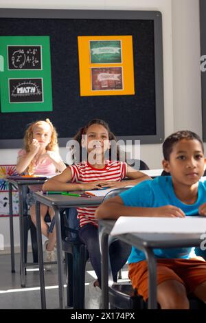 À l'école, groupe diversifié de jeunes étudiants assis à des bureaux dans la salle de classe avec espace de copie Banque D'Images