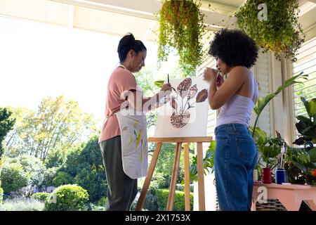 Femme biraciale mature et jeune femme biraciale peignant ensemble sur le porche à la maison Banque D'Images