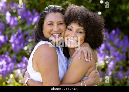 Mère et fille, femme mature biraciale et jeune femme embrassant, souriant à la maison dans le jardin Banque D'Images