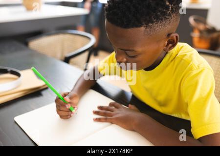 Garçon afro-américain dessinant à table, concentré sur le papier Banque D'Images