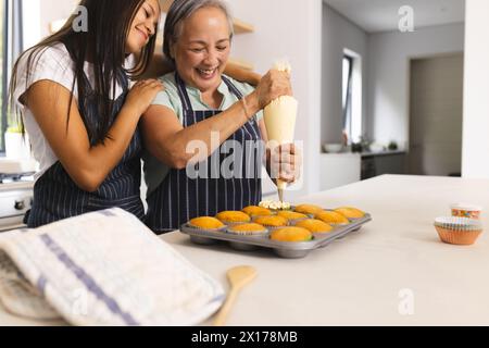 La grand-mère asiatique et la petite-fille adolescente biraciale décorent des cupcakes à la maison Banque D'Images