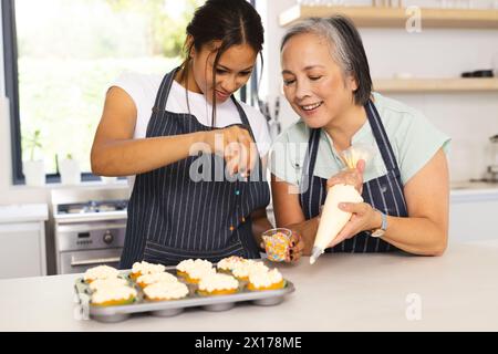 La grand-mère asiatique et la petite-fille adolescente biraciale décorent des cupcakes à la maison Banque D'Images