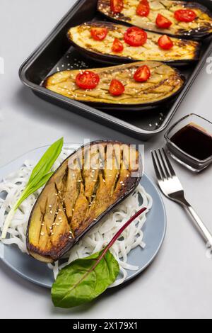 Aubergines cuites au four avec des légumes verts et des nouilles de riz sur l'assiette. Aubergines cuites au four avec tomates en palette. Sauce dans un bol en verre. Vue de dessus Banque D'Images