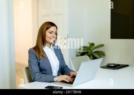 Femme professionnelle concentrée travaille avec diligence sur son ordinateur portable, son espace de travail baigné de lumière naturelle. Banque D'Images