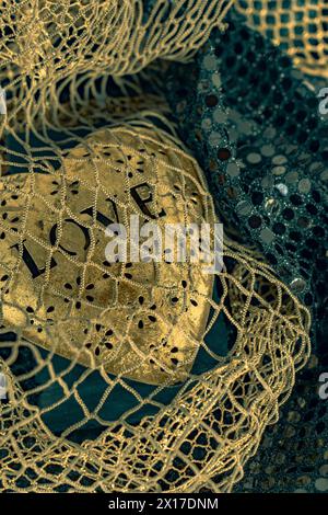 Cœur en métal doré brillant brillant lumineux est attrapé dans la mer d'amour de filet de poisson. L'arrière-plan est bleu bokeh. La lumière se reflète sur la sculpture en forme de coeur. Lueurs métalliques. Banque D'Images
