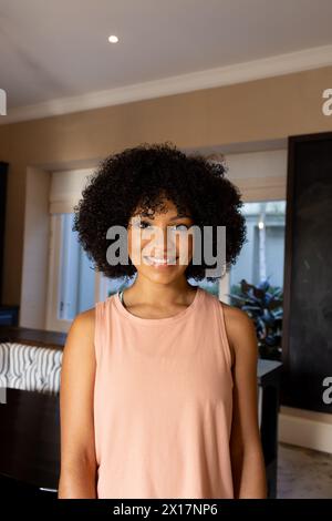 Jeune femme biraciale debout à l'intérieur, souriant à la caméra à la maison Banque D'Images