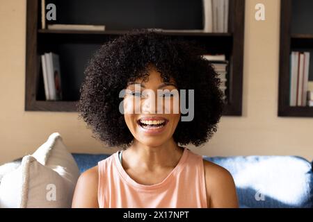 Jeune femme biraciale avec les cheveux noirs bouclés souriant à la maison Banque D'Images