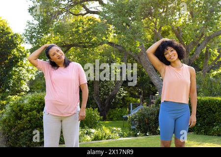 Femme biraciale mature et jeune femme biraciale s'étirant dans le parc à la maison Banque D'Images