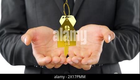 Image de clés de maison dorées et porte-clés en forme de maison tournant sur les mains coupées d'un homme caucasien 4K. Banque D'Images