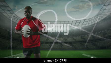 Image d'un joueur de rugby afro-américain debout, jouant avec une balle et regardant la caméra w Banque D'Images