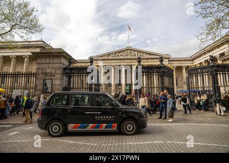 Londres, Angleterre - L'entrée emblématique du British Museum avec des visiteurs et un taxi noir classique au premier plan par temps nuageux. Banque D'Images