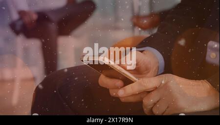 Image de neige tombant et des points lumineux sur un homme d'affaires caucasien utilisant un smartphone Banque D'Images