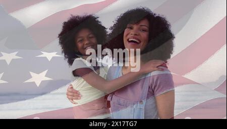 Image composite du drapeau américain sur la mère afro-américaine et sa fille souriant à la plage Banque D'Images