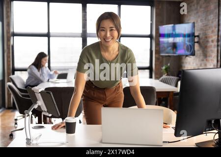 Professionnel mature asiatique debout par ordinateur portable, jeune collègue caucasien derrière Banque D'Images