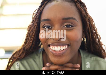 Femme afro-américaine aux cheveux tressés, souriant à la caméra à la maison Banque D'Images