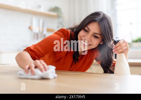 Femme souriante pulvérisant du nettoyant sur le comptoir en bois Banque D'Images