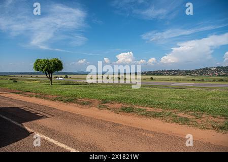 L'aéroport d'Entebbe, encadré par une végétation luxuriante, sous un ciel bleu clair avec des maisons lointaines, capture l'essence tranquille de l'Ouganda. Banque D'Images