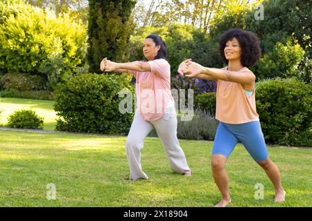 Femme biraciale mature et jeune femme biraciale exerçant dans le jardin à la maison, puis faisant du tai chi Banque D'Images