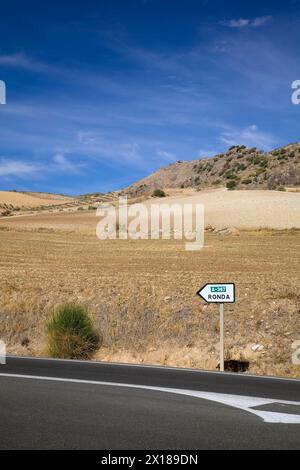 Route asphaltée noire et panneau routier au milieu d'un paysage aride indiquant la direction de Ronda, Espagne Banque D'Images