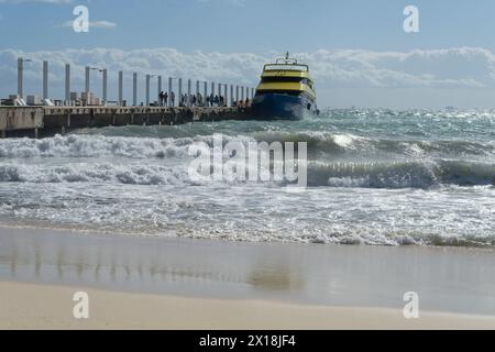 Un ferry amarré à un quai bondé de touristes sous un ciel lumineux, avec les vagues qui s'écrasent de la mer des Caraïbes à Playa del Carmen au Mexique Banque D'Images