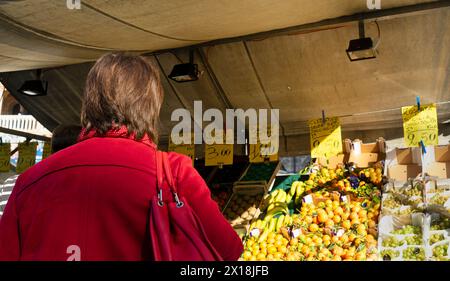 Femme au marché extérieur avec des fruits frais sous une tente, atmosphère animée et étiquettes de prix clairement visibles, dans une place dans le centre historique de Padoue, Banque D'Images