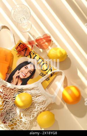 Sac à ficelle avec des fruits frais, magazine de mode et accessoires de plage sur fond beige, pose plate Banque D'Images